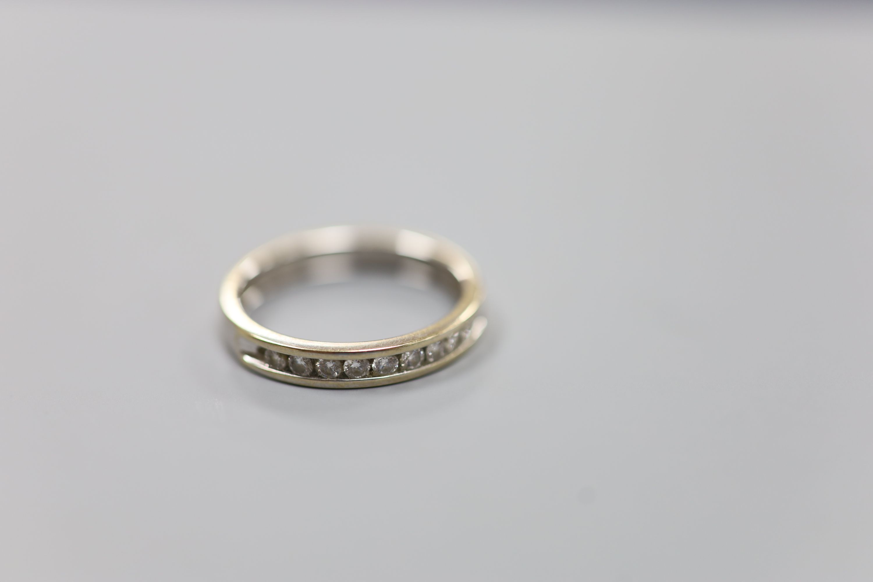 A modern 18ct white gold (worn) and nine stone channel set diamond half eternity ring, size P